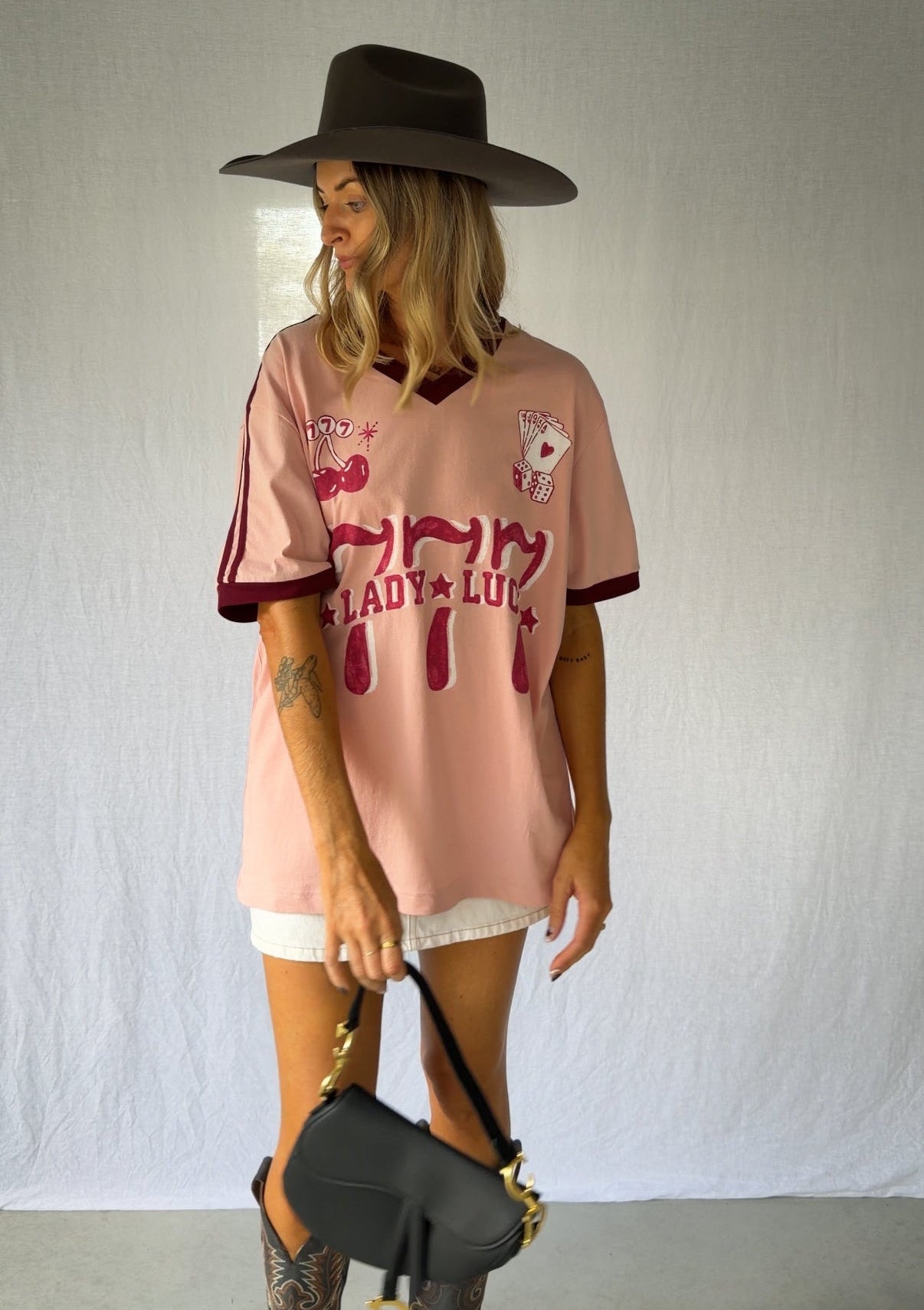 the Lucky Girl Tee is all about confidence, intuition, and calling in good things. Inspired by lucky motifs and the angel number 777, this women’s graphic tee blends playful symbolism with a bold, feminine edge. Pink base with burgundy trim for a flattering contrast. Jersey style vintage cotton.
The artist hand drawn art  western-style numbers and star detailing, finished with cherries, playing cards and dice graphics for a nostalgic, Americana-inspired feel.