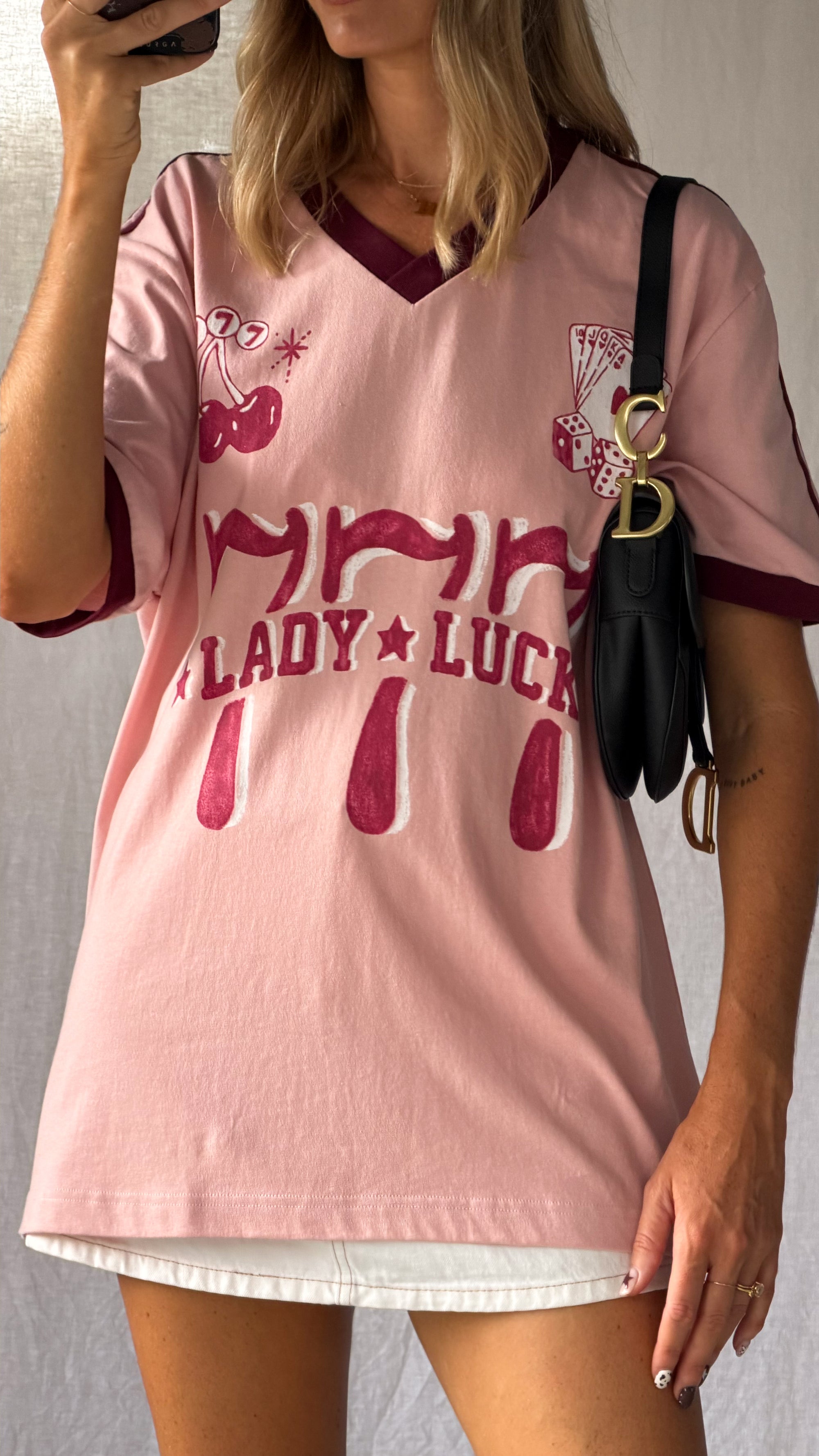 the Lucky Girl Tee is all about confidence, intuition, and calling in good things. Inspired by lucky motifs and the angel number 777, this women’s graphic tee blends playful symbolism with a bold, feminine edge. Pink base with burgundy trim for a flattering contrast. Jersey style vintage cotton.
The artist hand drawn art  western-style numbers and star detailing, finished with cherries, playing cards and dice graphics for a nostalgic, Americana-inspired feel.